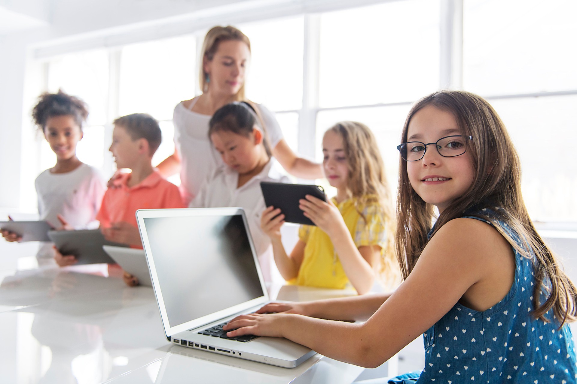 child with technology tablet and laptop computer in classroom teacher on the background